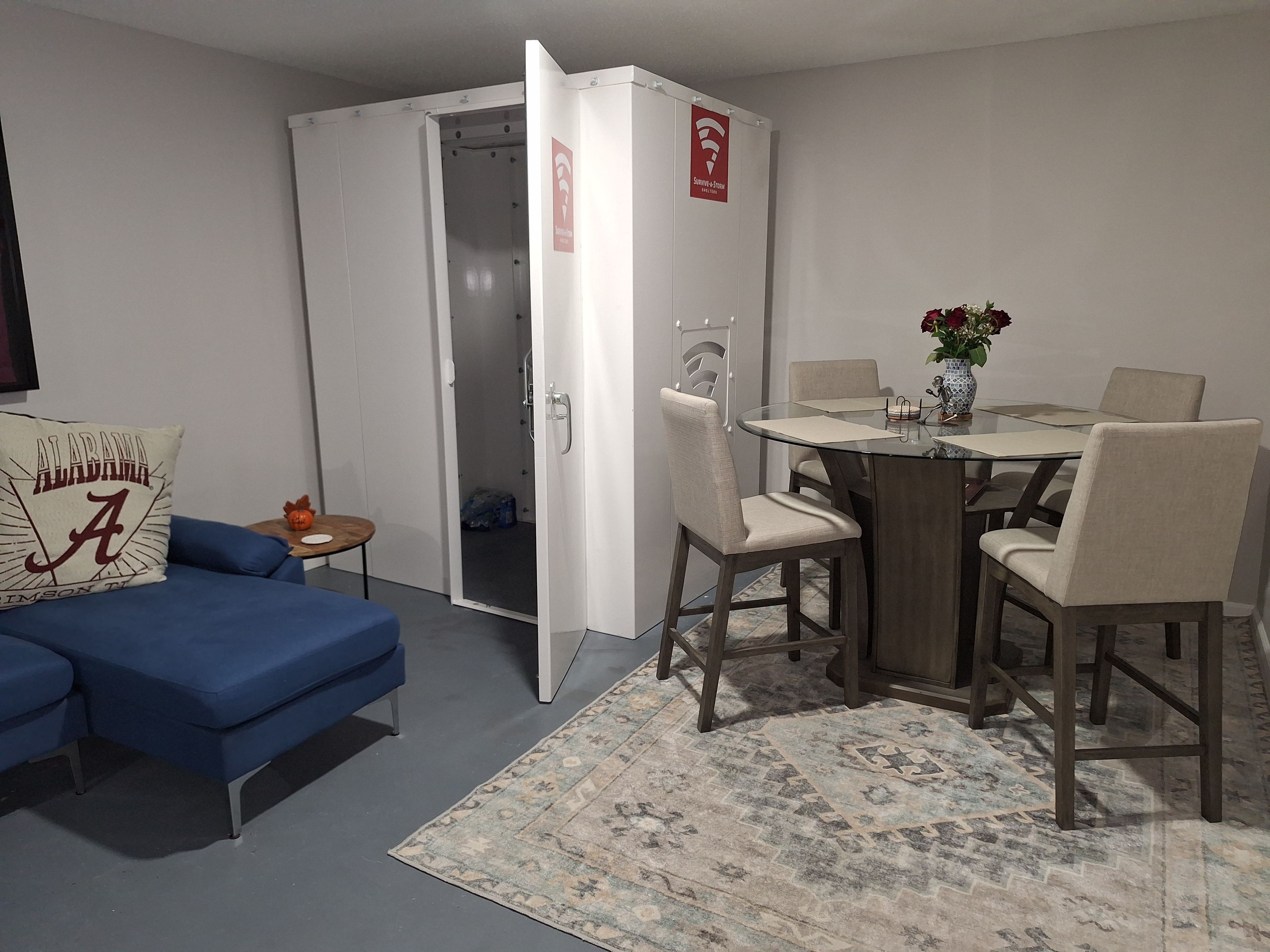 A room with a blue sofa, a dining table with chairs, a patterned rug, and a white wardrobe with a red emergency exit sign.