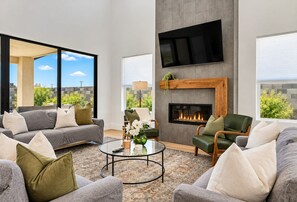A modern living room with a fireplace, comfortable seating, and a large window offering a city view. - Hurricane Hideaway - Hot Tub + Ping Pong - Pet Ok! (Hurricane)