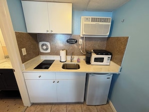Una cocina compacta con un lavamanos, un microondas, un refrigerador pequeño y un ventilador.