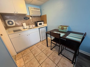 Cocina compacta con armarios blancos, microondas, refrigerador pequeño y una mesa de comedor con sillas.