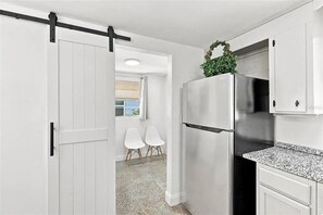 Eine Küche mit einem Edelstahl-Kühlschrank, weißen Schränken und einer Schiebetür im Bauernhausstil.