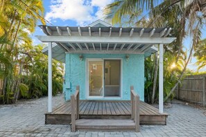 Un espace extérieur abrité doté d’une terrasse en bois, d’une porte-fenêtre coulissante et d’une pergola blanche.
