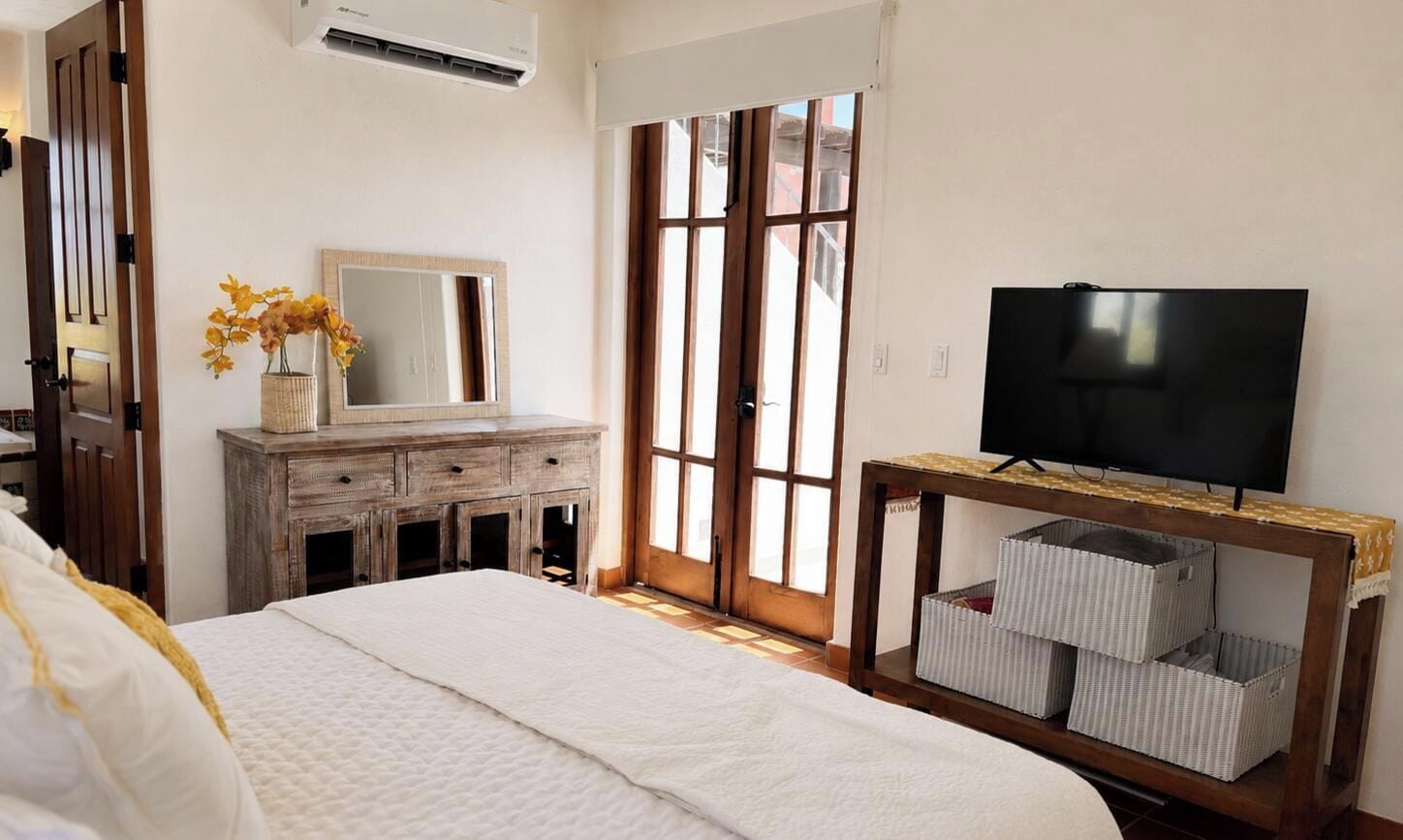 Un dormitorio con cama, cómoda, televisor sobre un mueble bajo y ventana con vistas.