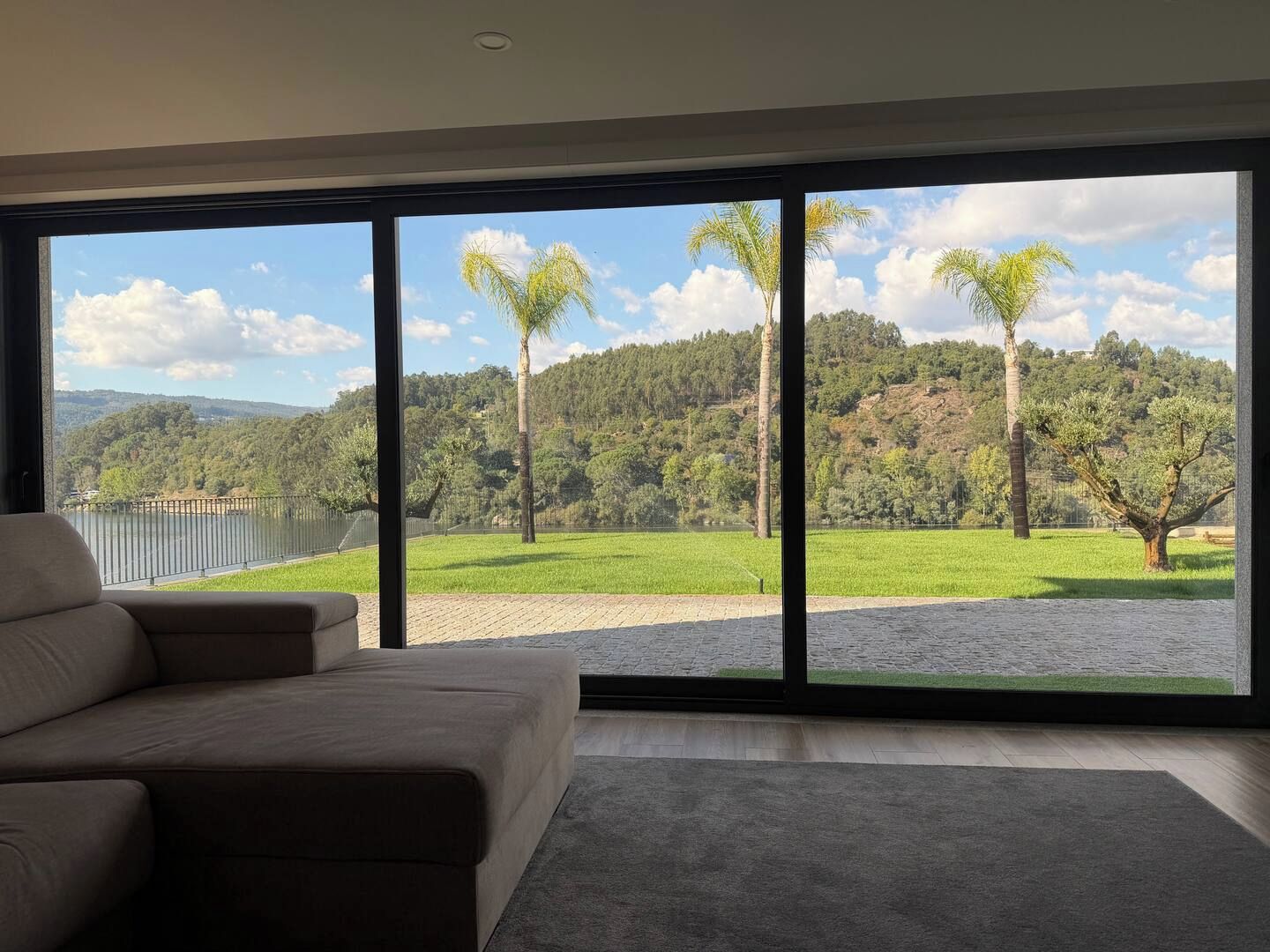 A modern living room with a large window overlooking a scenic landscape, including a lake and a forested hill.