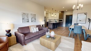 A modern living room with a sofa, coffee table, and dining area. - Switchback Creek Two #5 | 3 Peaks Rentals (Sun Peaks)