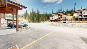 A parking area with a building in the background, surrounded by trees. - Switchback Creek Two #5 | 3 Peaks Rentals (Sun Peaks)