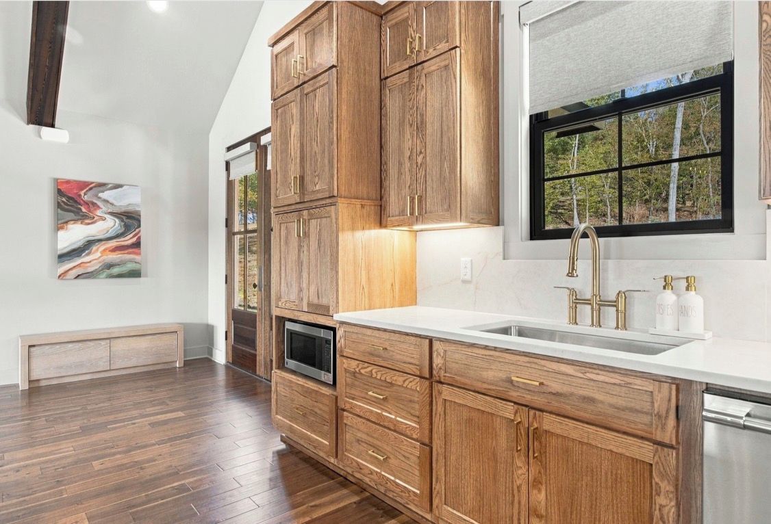 Una cocina con armarios de madera, un lavamanos de acero inoxidable y una ventana con vista a árboles.