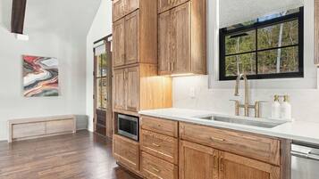 Una cocina con armarios de madera, un lavamanos de acero inoxidable y una ventana con vista a árboles.