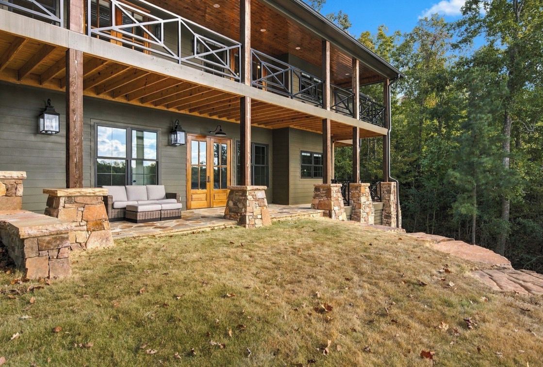 A two-story house with a stone fireplace, a covered porch, and a stone bench.