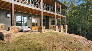 A two-story house with a stone fireplace, a covered porch, and a stone bench.