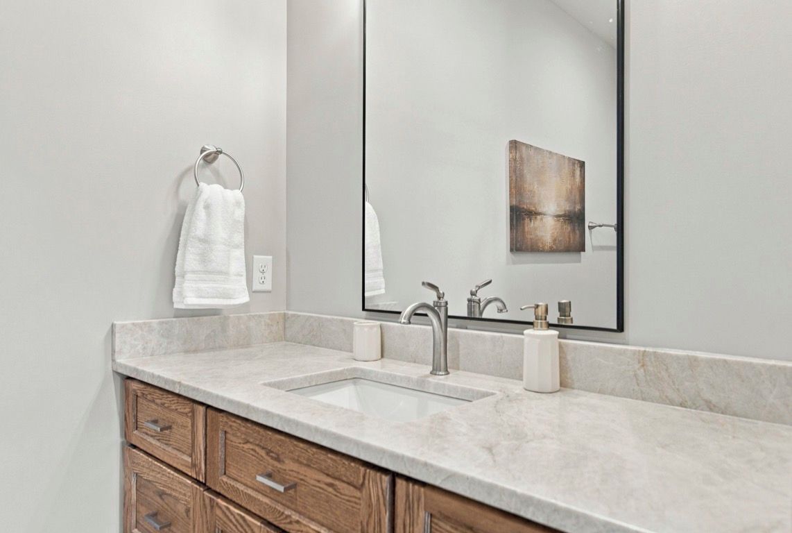 A bathroom with a marble countertop, a sink, a mirror, and wooden cabinetry.