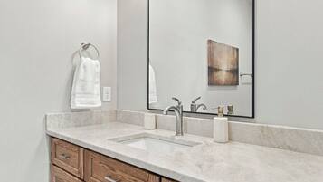 A bathroom with a marble countertop, a sink, a mirror, and wooden cabinetry.