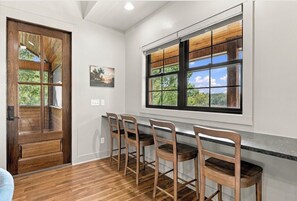 A kitchen with wooden bar stools, a large window with a view, and a wooden door.