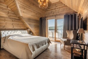 Ein Schlafzimmer mit einem großen Bett, einem Sessel, einem Tisch mit Lampe und Blick ins Freie.