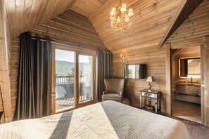 Een slaapkamer in een houten chalet met een groot bed, een stoel, een televisie en uitzicht op de omgeving.
