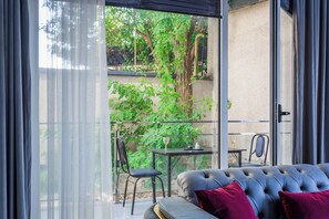 A balcony with a sofa, a table, and chairs, overlooking a garden with trees and a building in the background. - Apartments Zarafshan city 5 Tashkent (Tashkent)