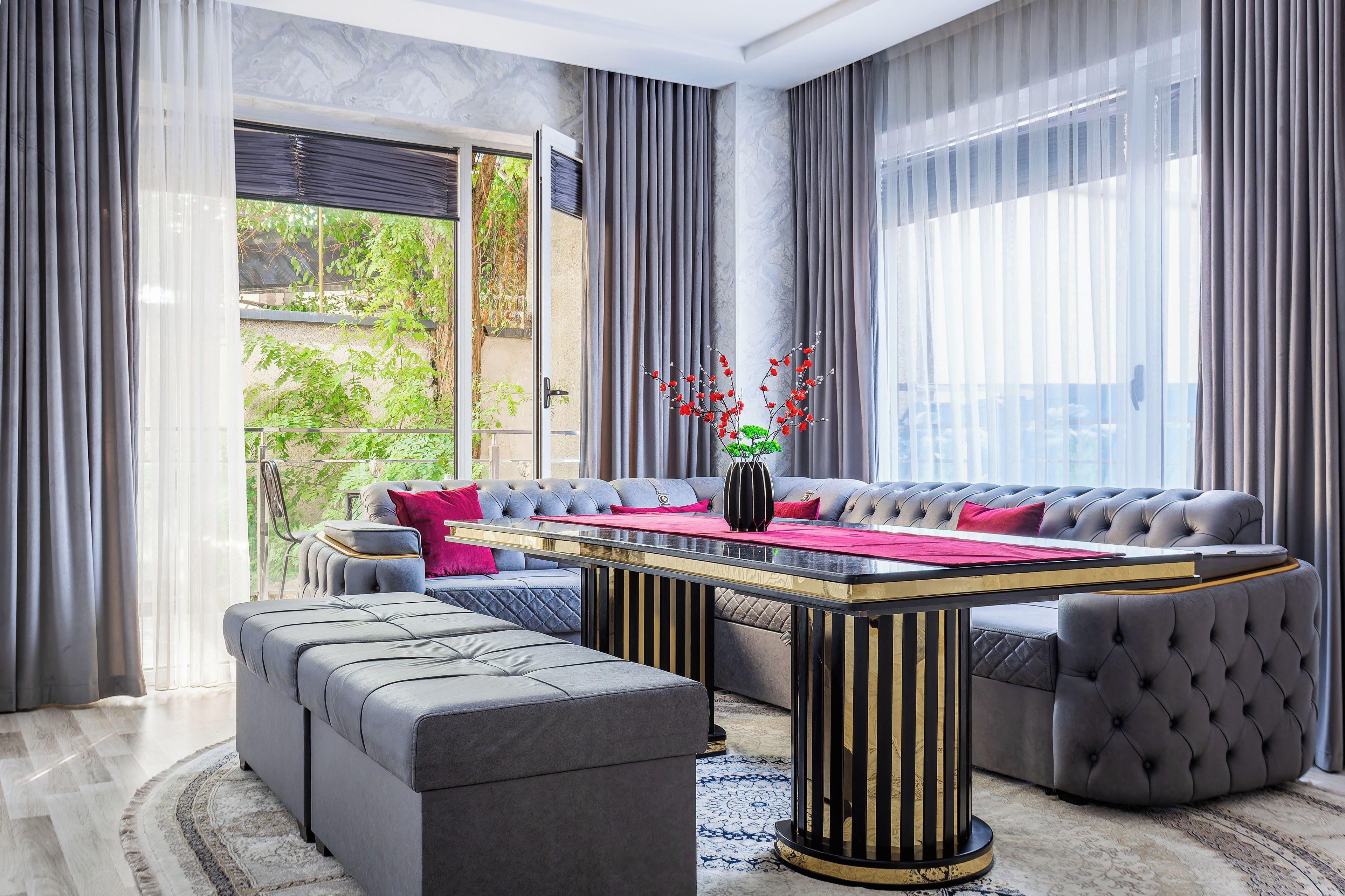 Una sala de estar moderna con un sofá modular, otomanas, una mesa de centro y un florero con flores rojas.