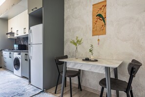 A modern kitchen with a built-in washing machine, a dining area with a table and chairs, and a decorative wall hanging. - Apartments Zarafshan city 5 Tashkent (Tashkent)