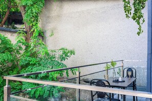 Un balcon agrémenté d’une table et de chaises, entouré de verdure et doté d’un mur à la texture particulière.