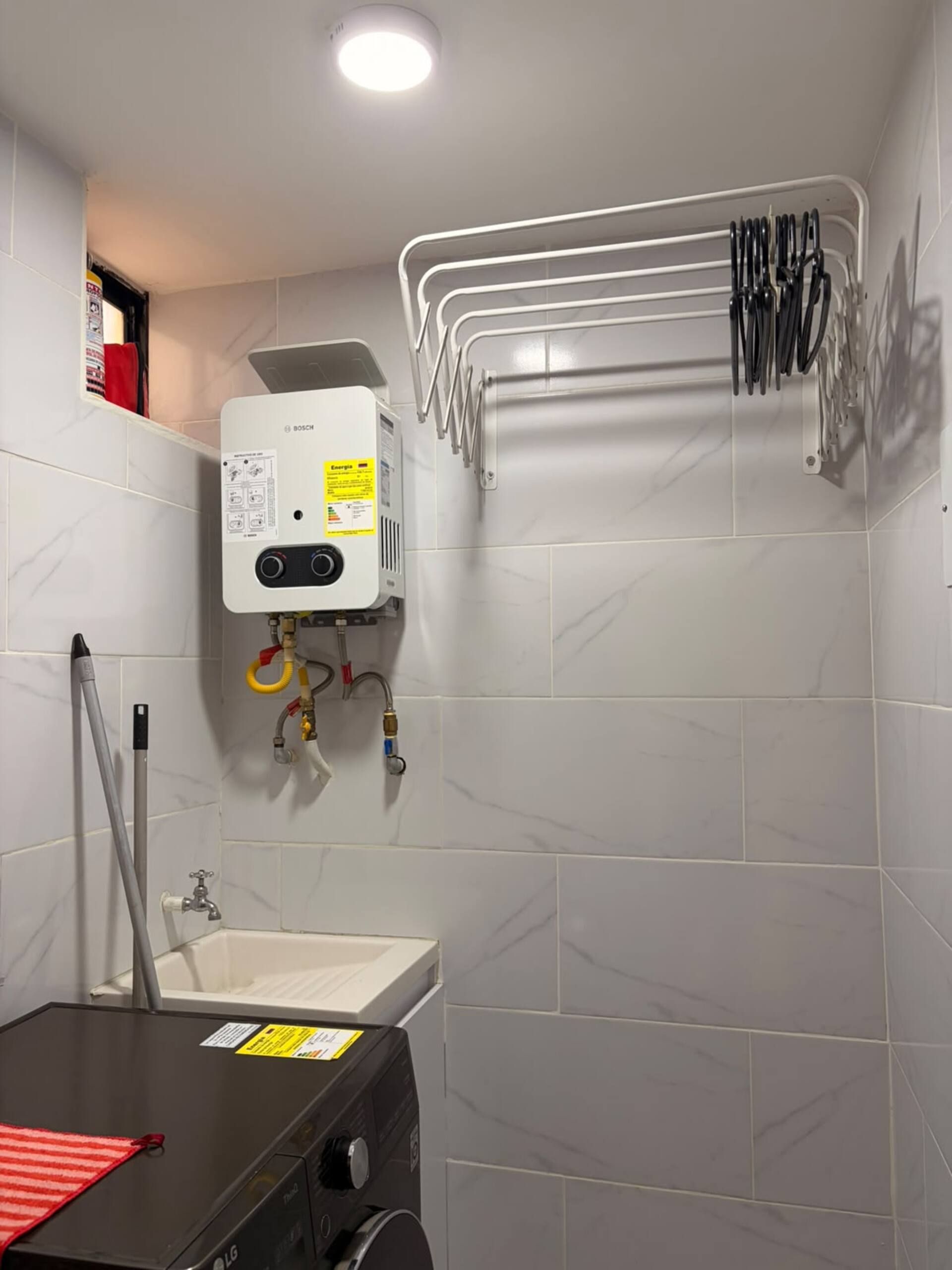 A bathroom with a Bosch water heater, a sink, and a towel rack with various cleaning tools.