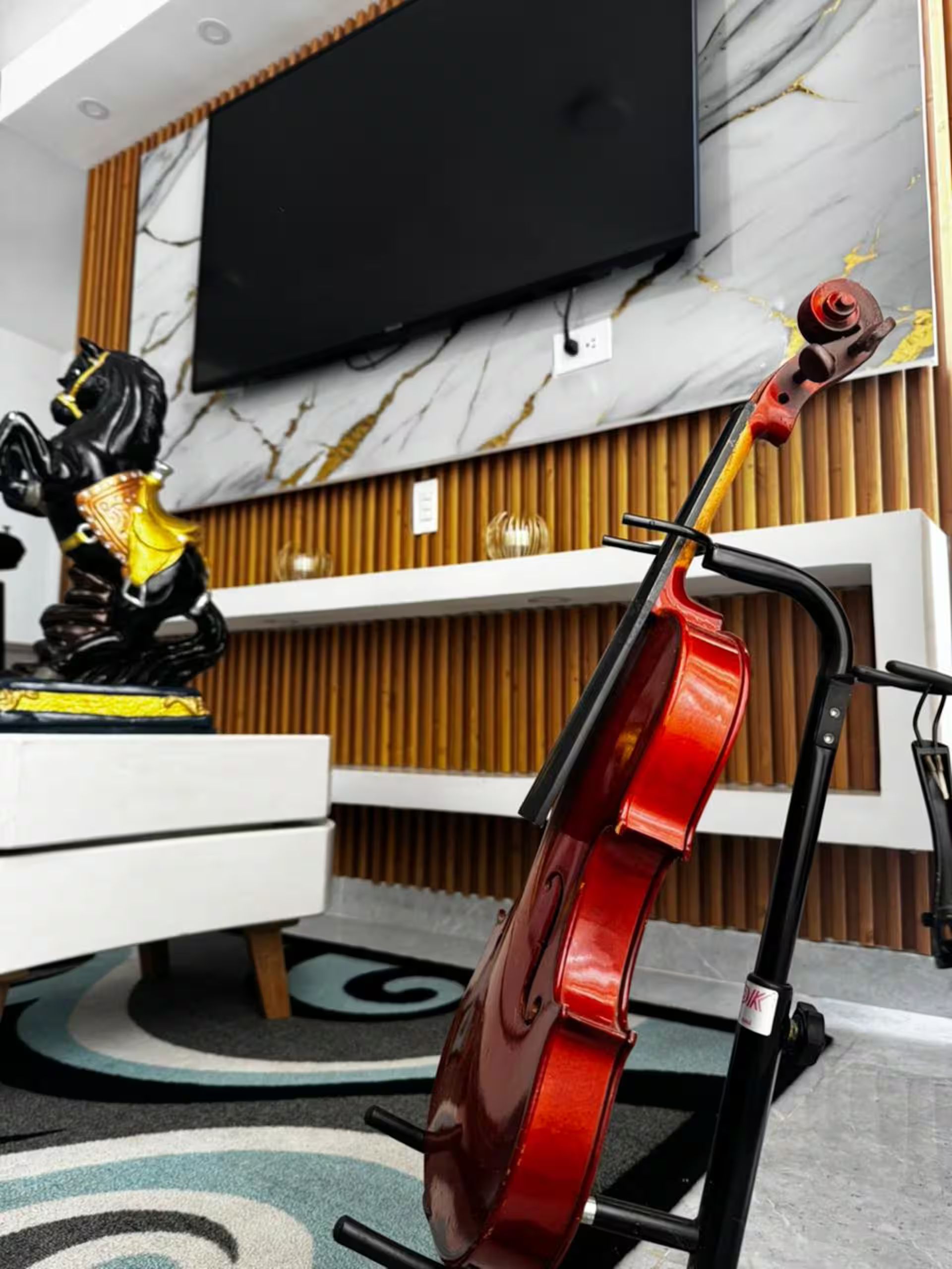 A modern living room with a mounted television, a red cello, and a decorative horse statue.
