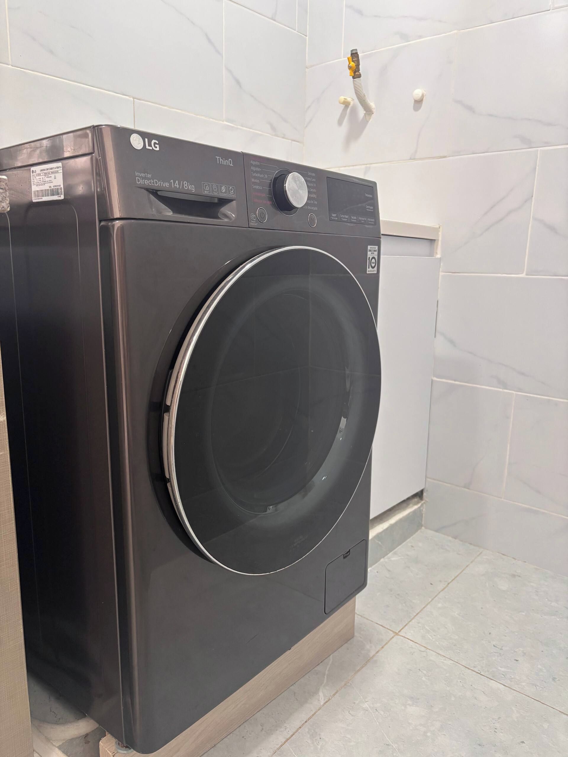 Een zwarte LG DirectDrive 14/81 wasmachine in een badkamer met witte marmeren tegels en een zichtbare waterleiding.