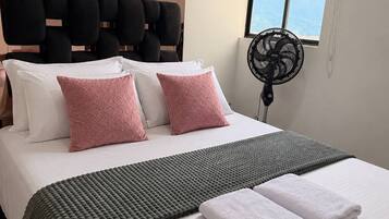 Een hotelkamer met een bed, kussens, dekens, een ventilator en een raam met uitzicht.