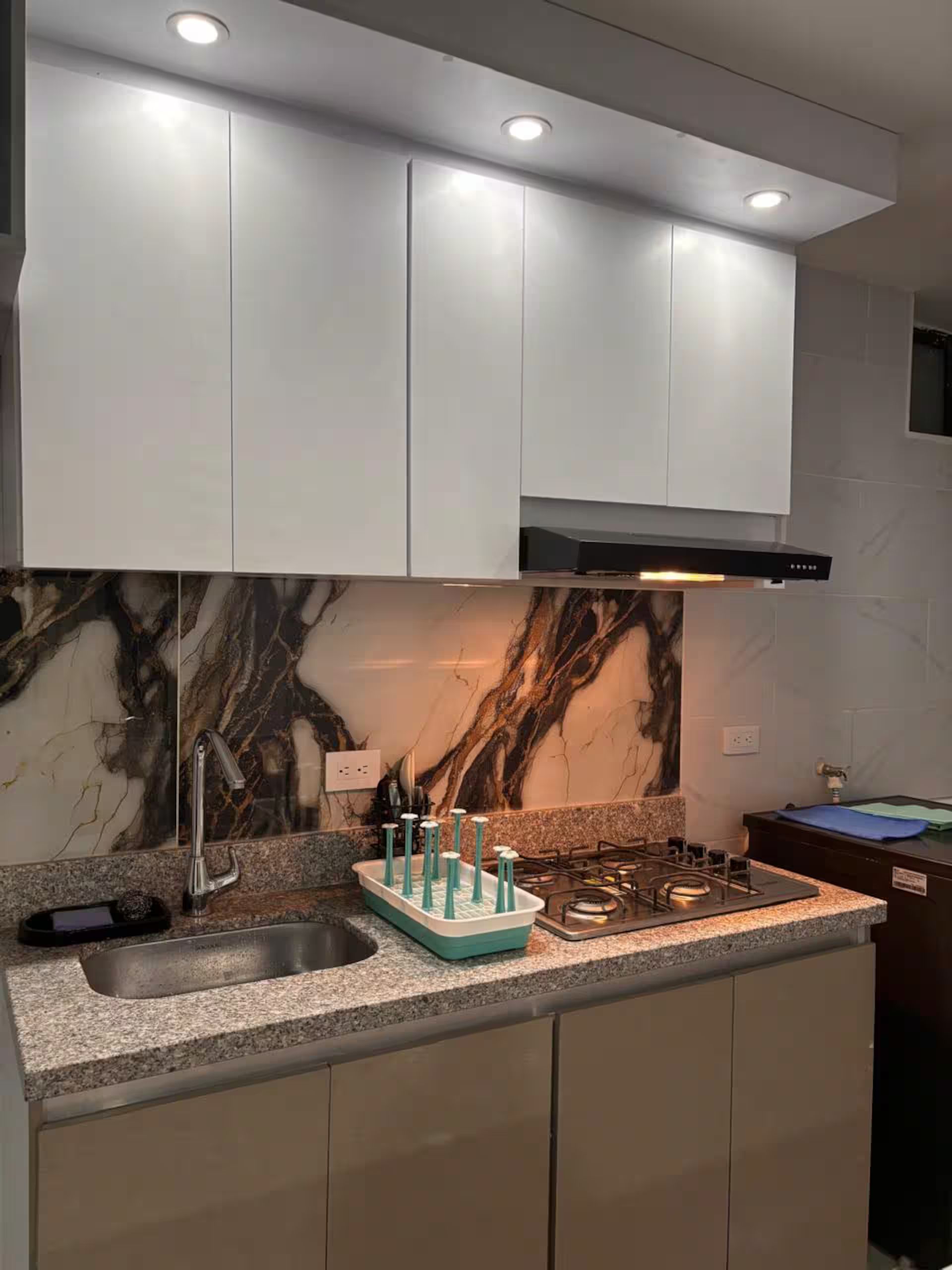 Una cucina moderna con un piano di lavoro in granito, lavello in acciaio inossidabile e piano cottura a gas.