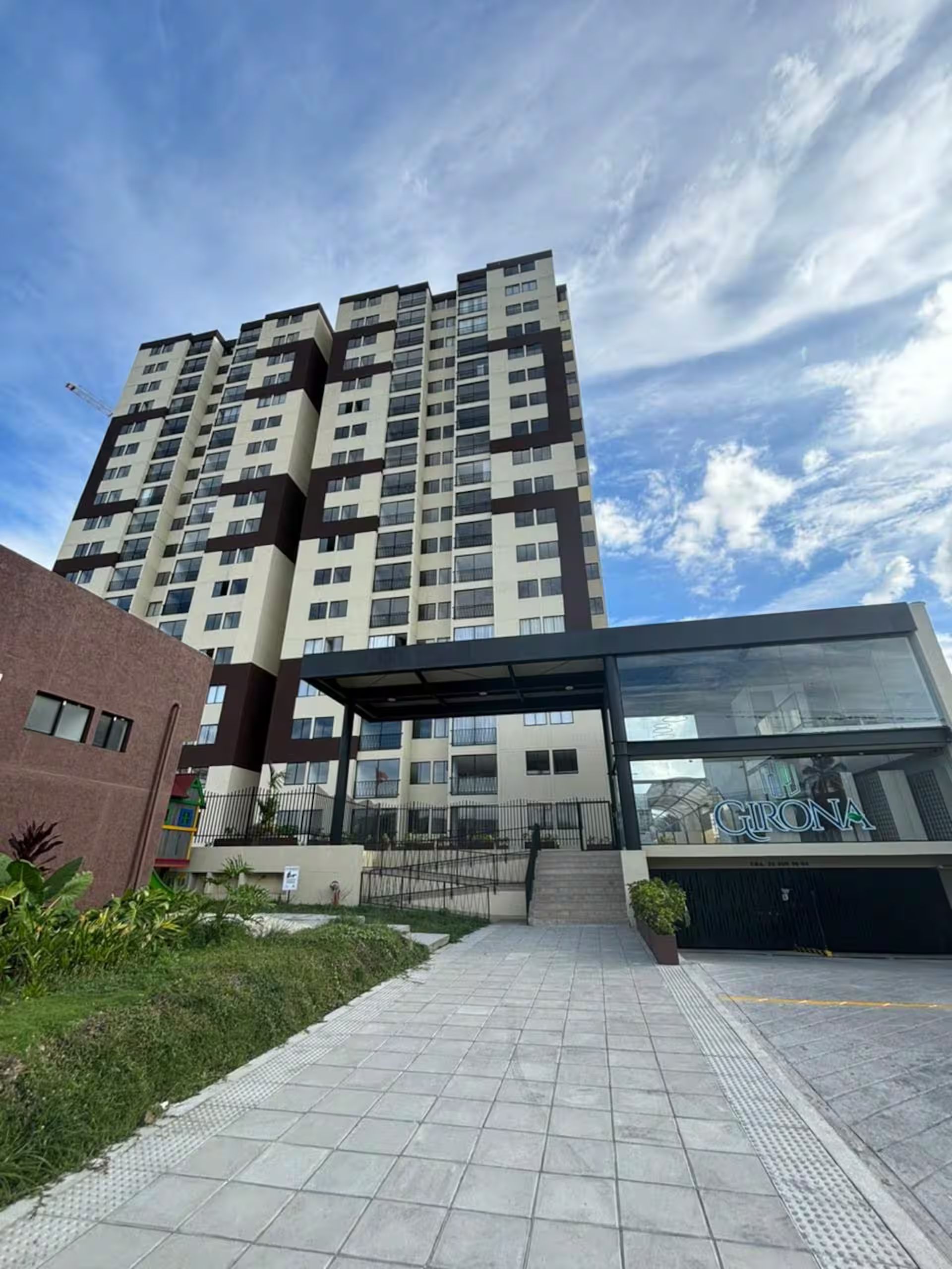 Een hoog appartementencomplex met een modern ontwerp, met een overdekte ingang en een zichtbaar logo.