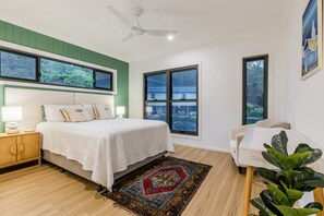 Ein Schlafzimmer mit Bett, Nachttischen, Deckenventilator, großen Fenstern und Blick ins Freie.