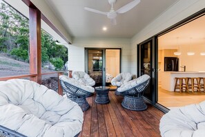 A covered outdoor seating area with cushioned chairs and a table, a ceiling fan, and a view of the surrounding landscape. - Coastal Haven | Boat Parking | Walk to Town (Agnes Water)