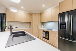 A modern kitchen with a built-in oven, stainless steel refrigerator, and a sleek island with a sink. - Coastal Haven | Boat Parking | Walk to Town (Agnes Water)