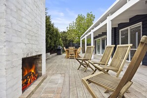 A patio with a fire feature, wooden furniture, and a covered area with windows. - Black Pearl (Rye)