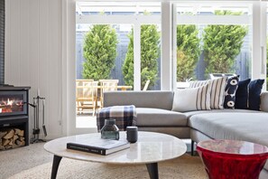 Ein Wohnzimmer mit Sofa, Couchtisch, Kamin und Blick ins Freie.