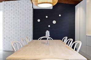 A dining area with a wooden table, white chairs, a white candle on a glass holder, and a black wall with circular decorations. - Black Pearl (Rye)