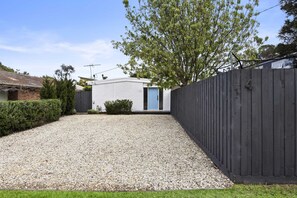 A residential property with a gravel driveway, a wooden fence, and a house with a blue door. - Black Pearl (Rye)