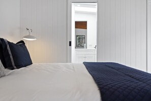 A bedroom with a bed, a bedside lamp, and a door leading to a bathroom. - Black Pearl (Rye)