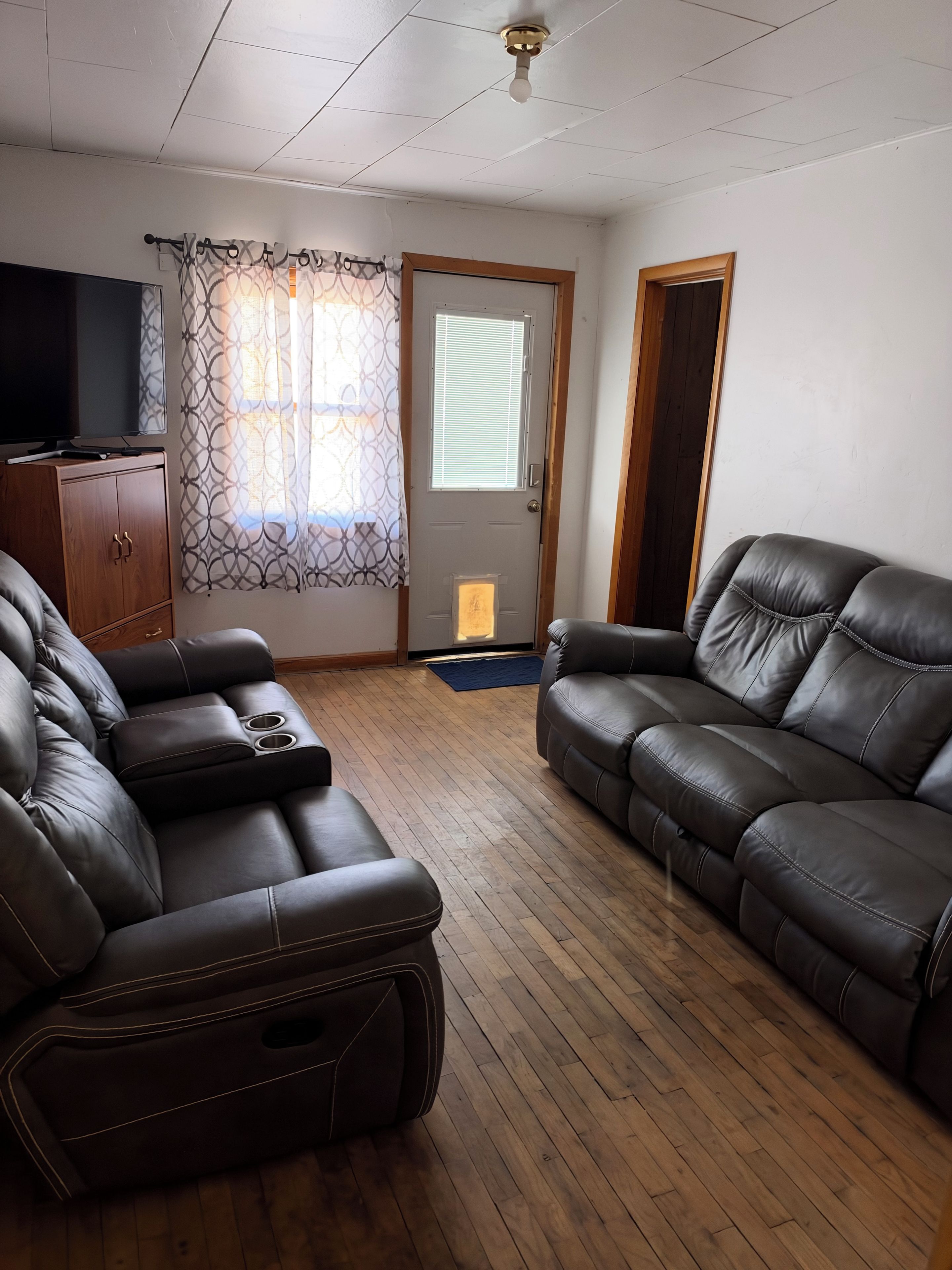 A living room with a sofa, a recliner, a wooden cabinet, and a television.
