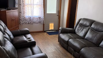 A living room with a sofa, a recliner, a wooden cabinet, and a television.