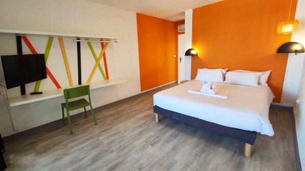 Una habitación de hotel con una cama, un escritorio con televisor, una silla y una pared con líneas coloridas.