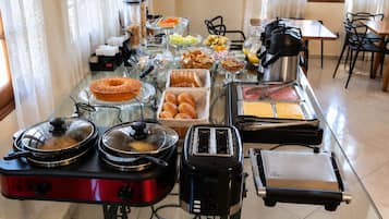 Montaje de bufé con diversos alimentos y aparatos como una cafetera, tostadora y un calentador de comida.