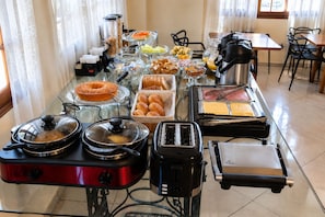 Montaje de bufé con diversos alimentos y aparatos como una cafetera, tostadora y un calentador de comida.