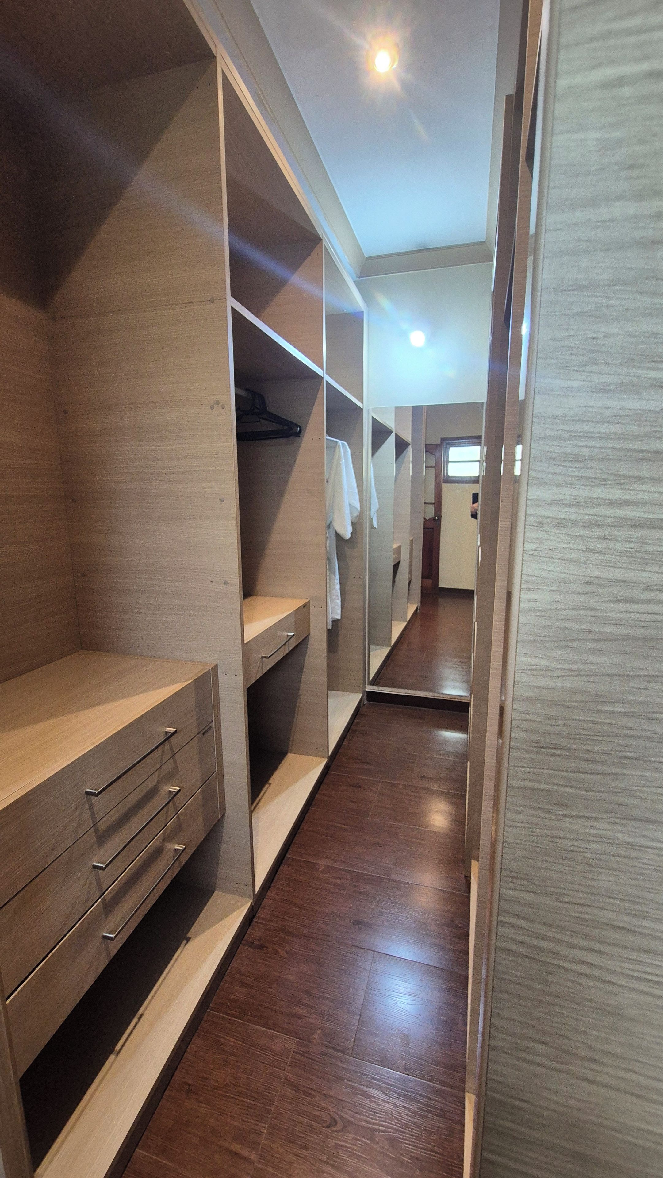 Un vestidor con estantes de madera, un espejo y una barra para colgar ropa.