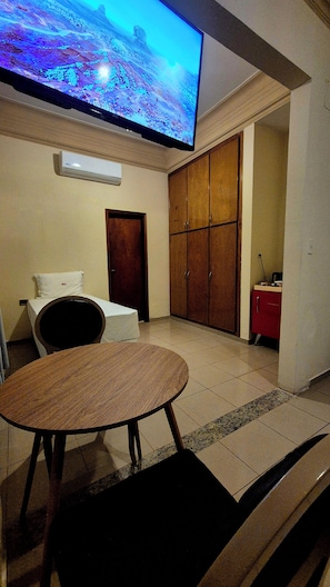 A room with a television mounted on the wall, a bed with a white mattress and pillow, a wooden table with a chair, and a wardrobe with multiple doors. - Hibisco Hotel Boutique (Encarnación)