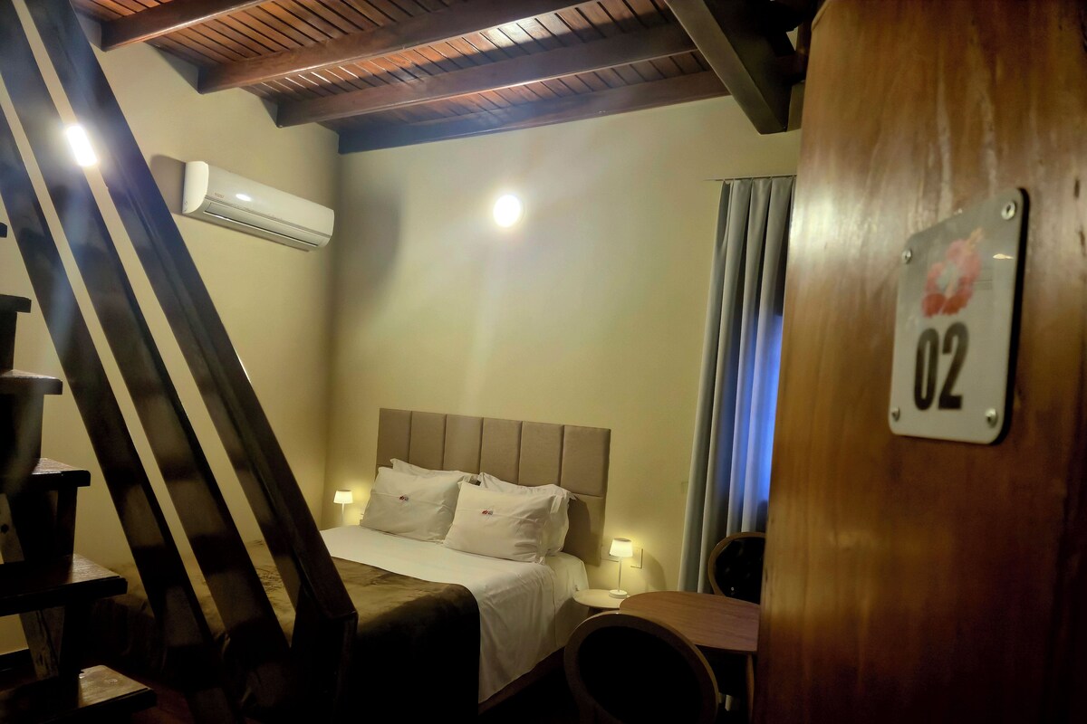 A hotel room with a bed, a desk, a chair, an air conditioning unit, and a number sign.