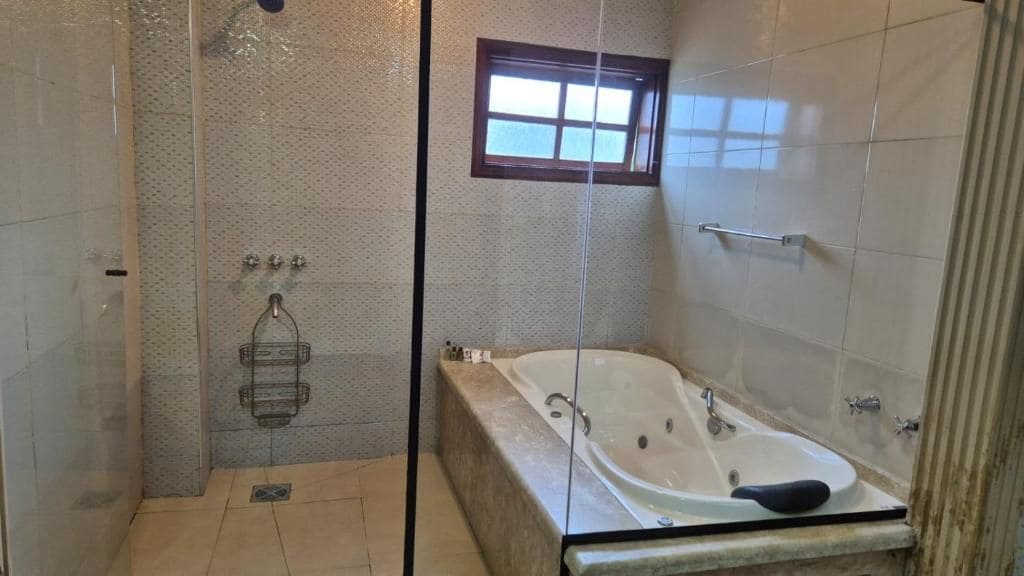 A bathroom with a glass-enclosed shower, a bathtub, and a small window.