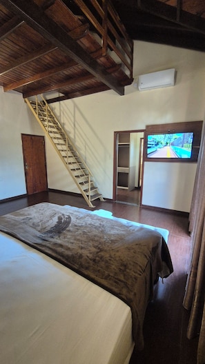 A bedroom with a bed, a wooden staircase, a television, and a closet.