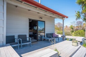 Une terrasse extérieure couverte, dotée d’un espace salon et d’une porte-fenêtre coulissante donnant accès à un espace intérieur.
