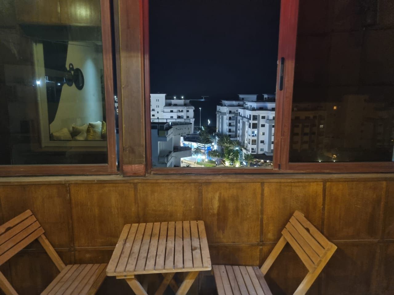 A balcony with wooden furniture and a view of a cityscape at night.