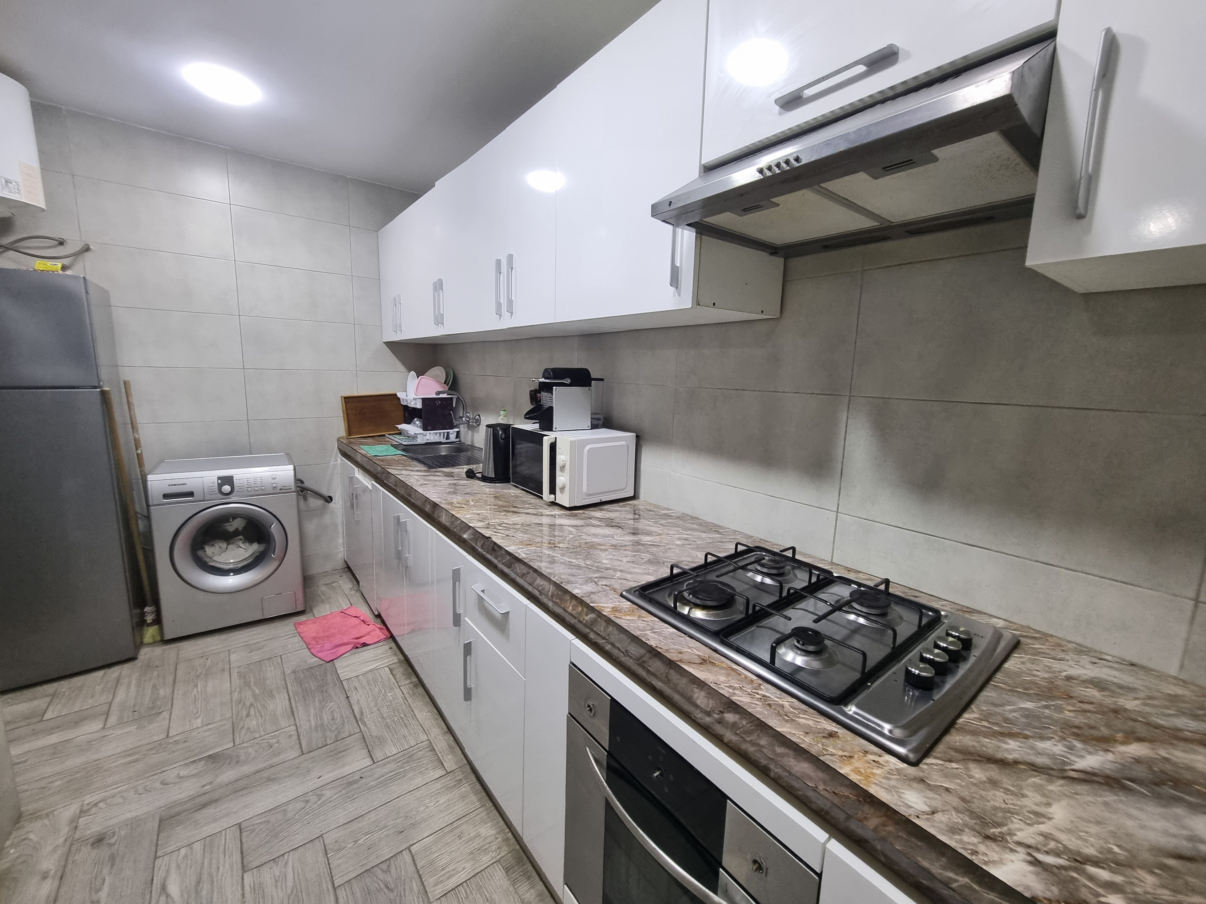 A compact kitchen with a built-in washing machine, a microwave, a gas stove, and white cabinets.